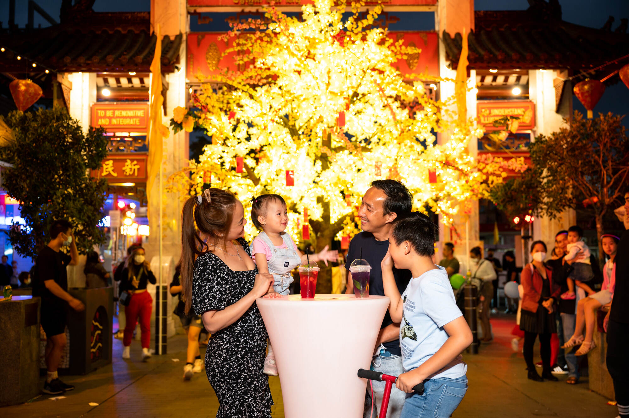 Young family in front of lit up money tree at night-time