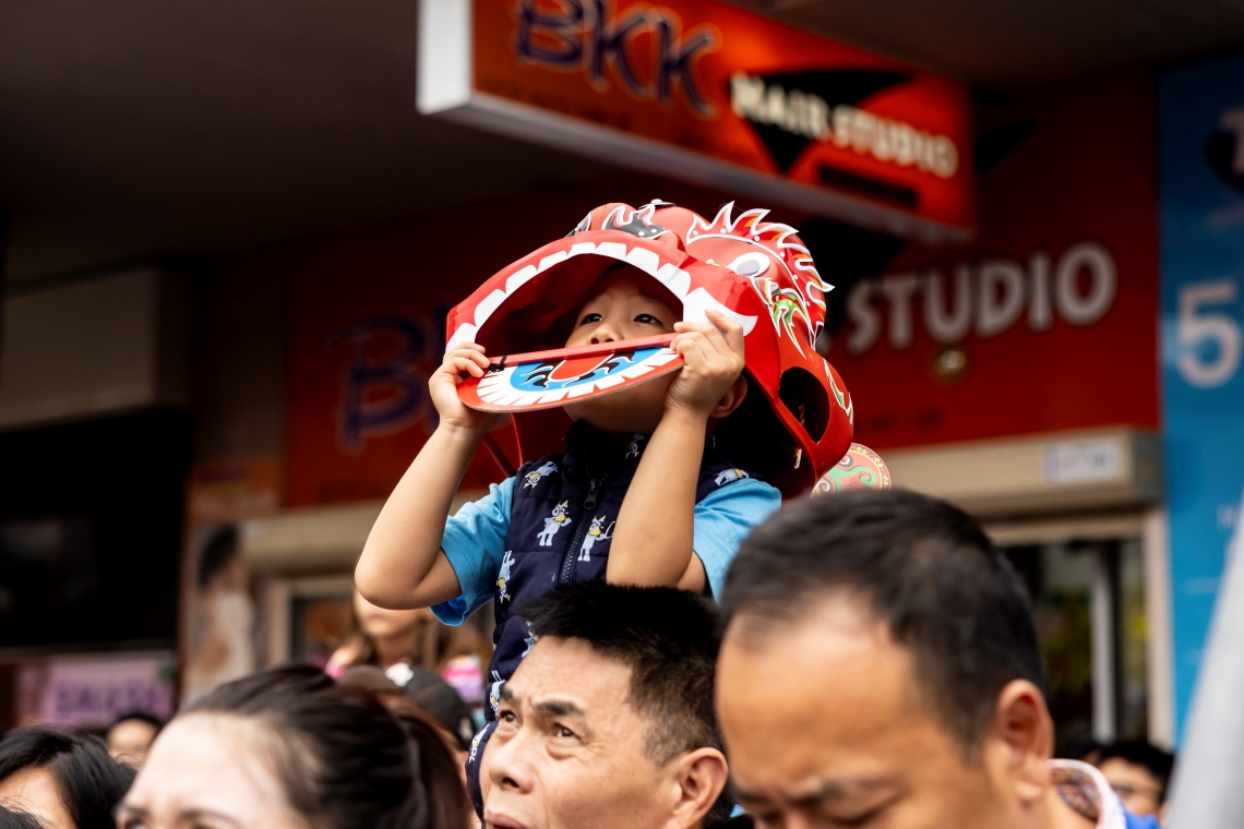 Boy wearing lion head craft in crowd at Lunar New Year.