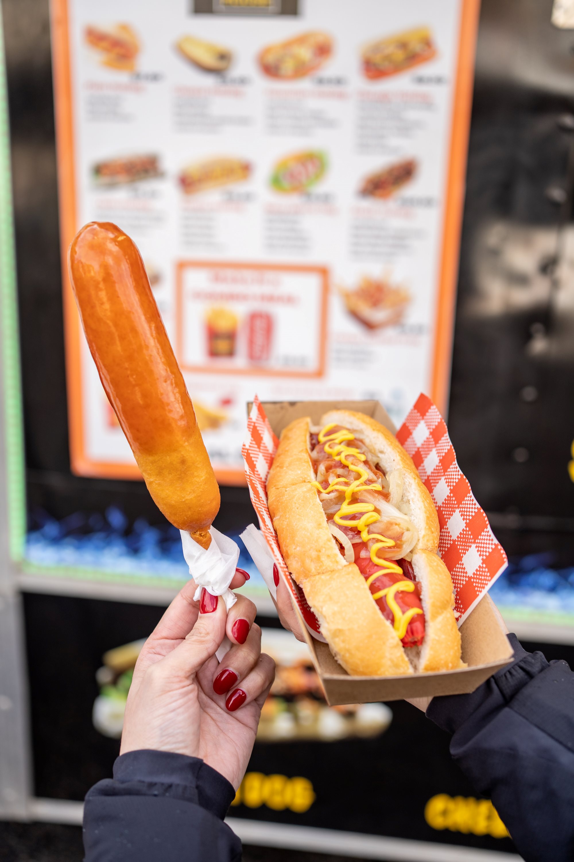 Hot-dog-and-corn-dog-being-held-in-front-of-food-truck-menu-board